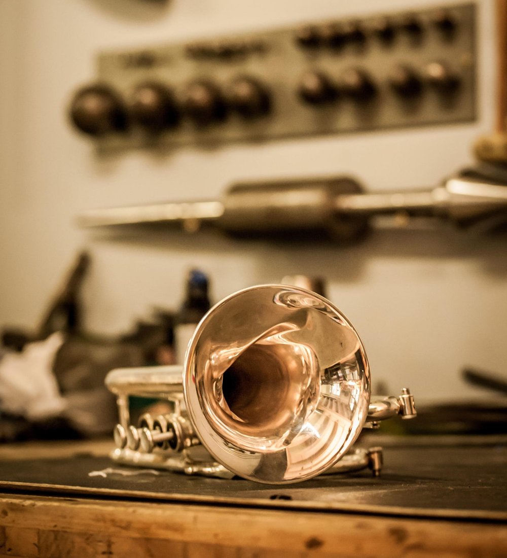A trumpet on a repair workbench with tools hanging on the wall behind it